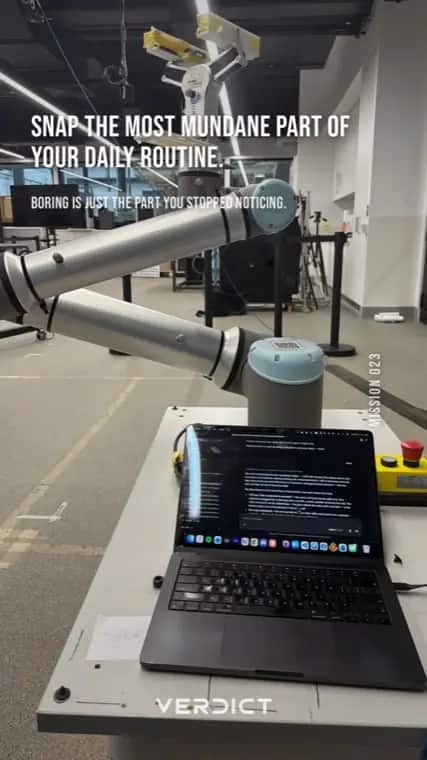 Verdict mission 23, "Snap the most mundane part of your daily routine.", answered with an industrial robot arm beside a laptop on a lab bench.
